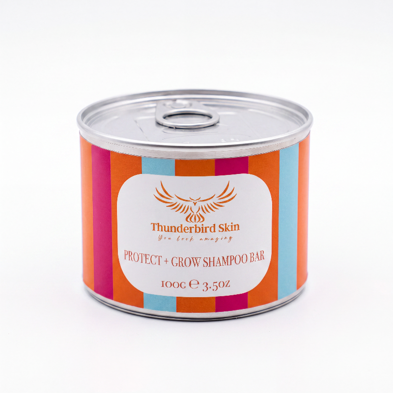 A cylindrical metal can of Thunderbird Skin Protect + Grow Shampoo Bar, featuring a colorful label with vertical stripes of orange, pink, and light blue around a central white label with an eagle logo.
