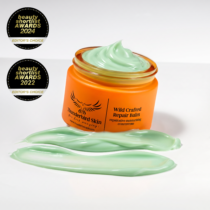 An open jar of Thunderbird Skin Wild Crafted Repair Balm with pale green balm cream visible inside and in front, set on a white background with two black beauty shortlist award badges on the left.